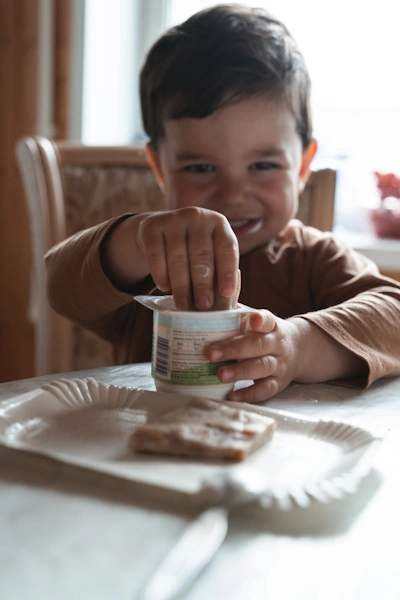 child sitting at table eating yoghurt and toast